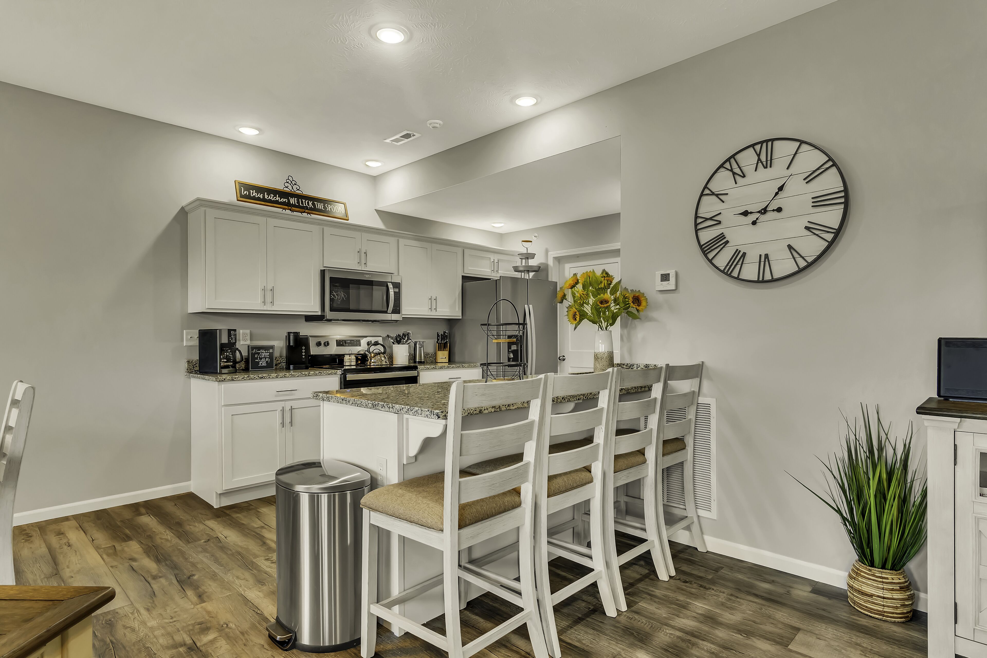 Une cuisine moderne avec des meubles blancs, une grande horloge et un coin repas avec des chaises blanches.