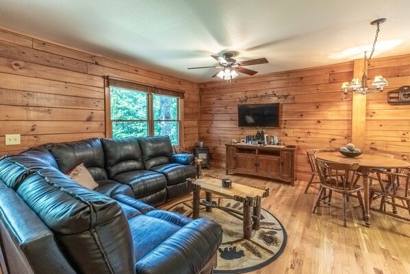A cozy cabin interior with a leather sofa, wooden dining table, and a ceiling fan.