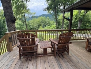 A wooden deck with two Adirondack chairs and a small table, overlooking a forested area. - Whippoorwill Lake – Dock, Hot Tub – Pet Friendly (Robbinsville)