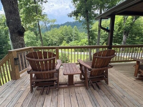 A wooden deck with two Adirondack chairs and a small table, overlooking a forested area.