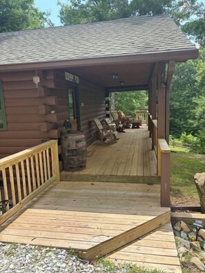 Une cabane en bois avec un porche, une pancarte de bienvenue et des sièges à l’extérieur.