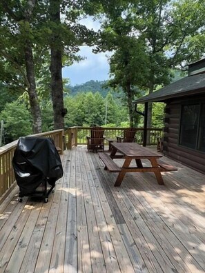 Une terrasse en bois avec des tables de pique-nique et un barbecue.