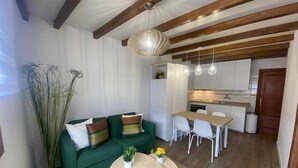 A modern living room with a green sofa, a small round table, and a dining area with a wooden table and white chairs.