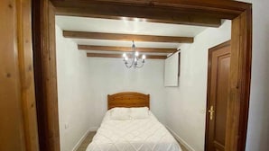 A bedroom with a wooden headboard, a white bedspread, a chandelier, and a wooden door.