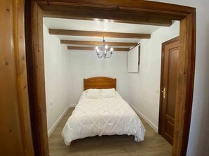 Quarto com cabeceira de madeira, colcha branca, lustre e porta de madeira.