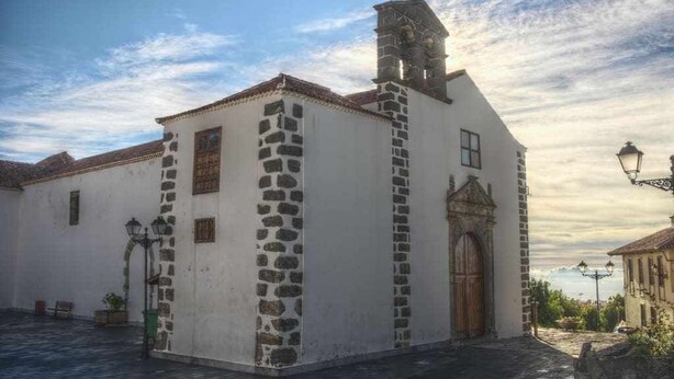 A white building with a stone facade, a bell tower, and a wooden door.