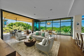 Relax in a spacious living area with a sofa, armchairs, and dining table, offering a view of lush greenery.
