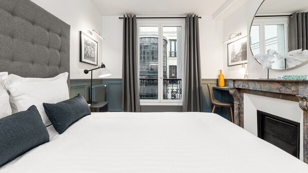 A modern hotel room with a large bed, a desk, a fireplace, and a view of the city through the window. - LivinParis | Luxurious 2 Bedroom Opera VI (Paris)