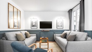 A modern living room with two grey sofas, a wooden coffee table, and a flat-screen TV mounted on the wall. - LivinParis | Luxurious 2 Bedroom Opera VI (Paris)