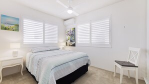 Un dormitorio con una cama, dos mesitas de noche, una silla y un ventilador de techo.