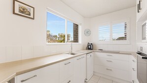 Una cocina moderna con armarios blancos, lavavajillas integrado y un amplio ventanal con vistas a la ciudad.