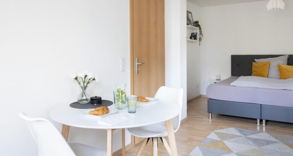 Un appartamento moderno con zona pranzo, un letto con testiera grigia e una porta in legno.