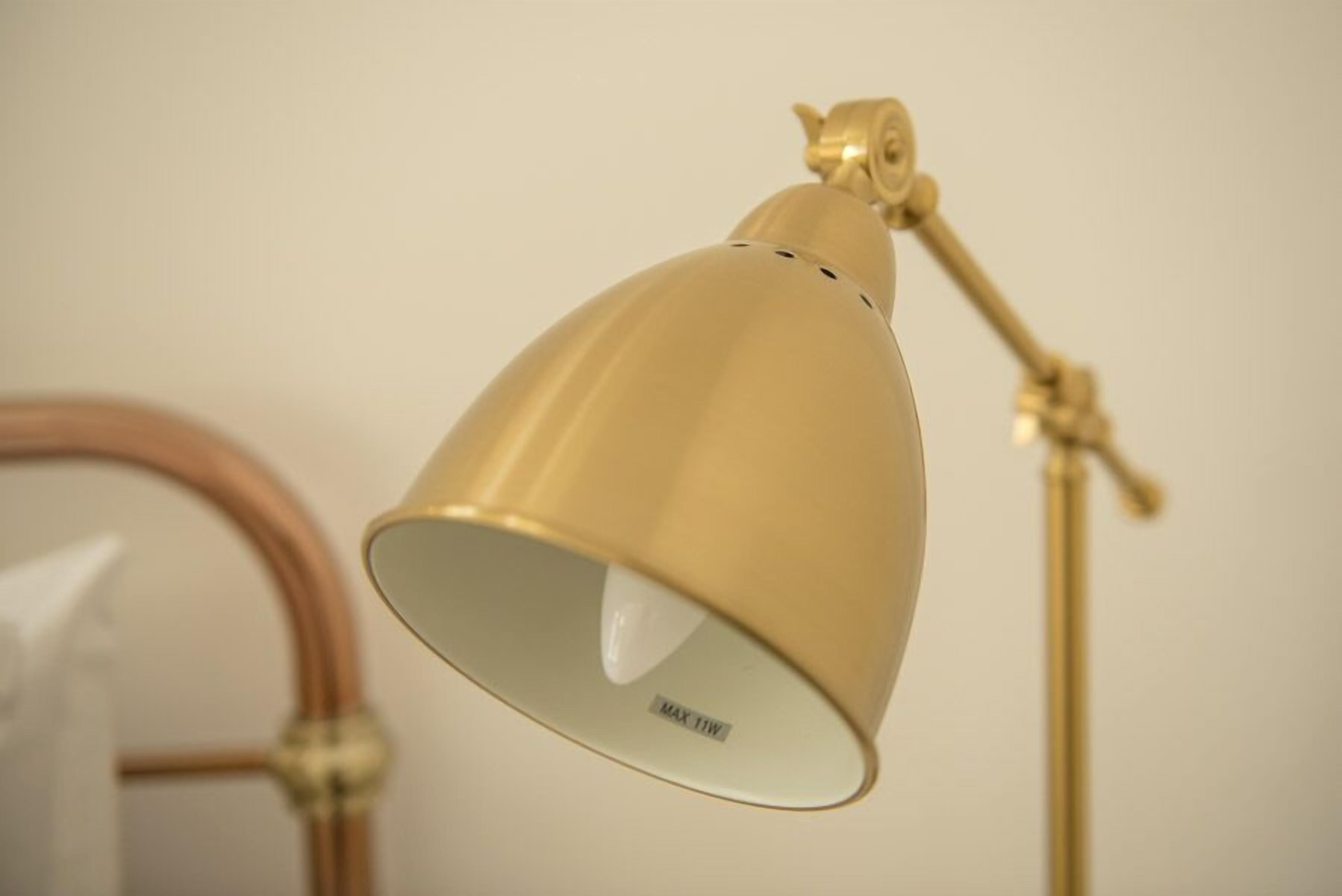 Une lampe de bureau de couleur dorée, dotée d’un abat-jour blanc et d’une étiquette indiquant « MAX 15 W ».