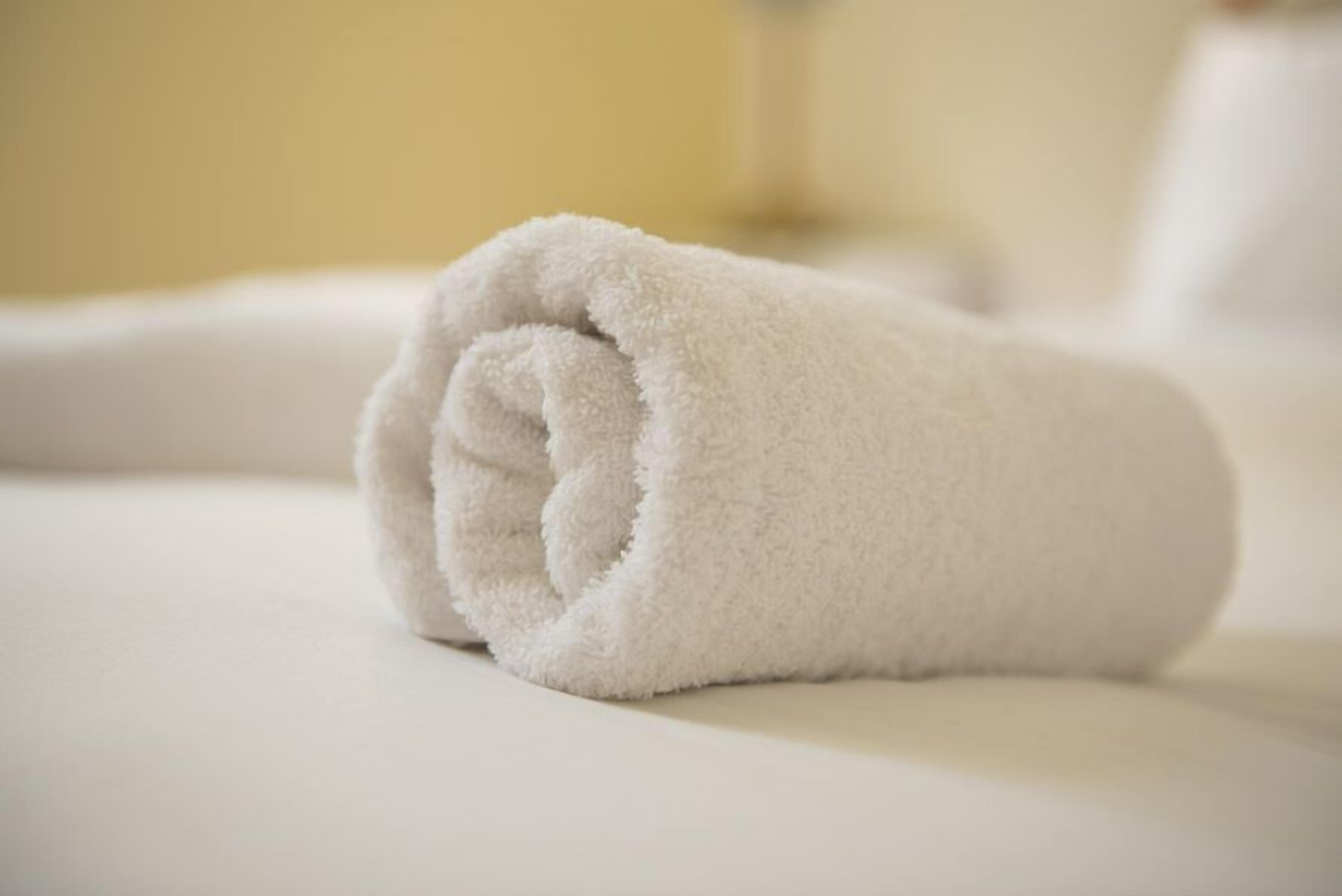 A neatly rolled white towel on a bed.