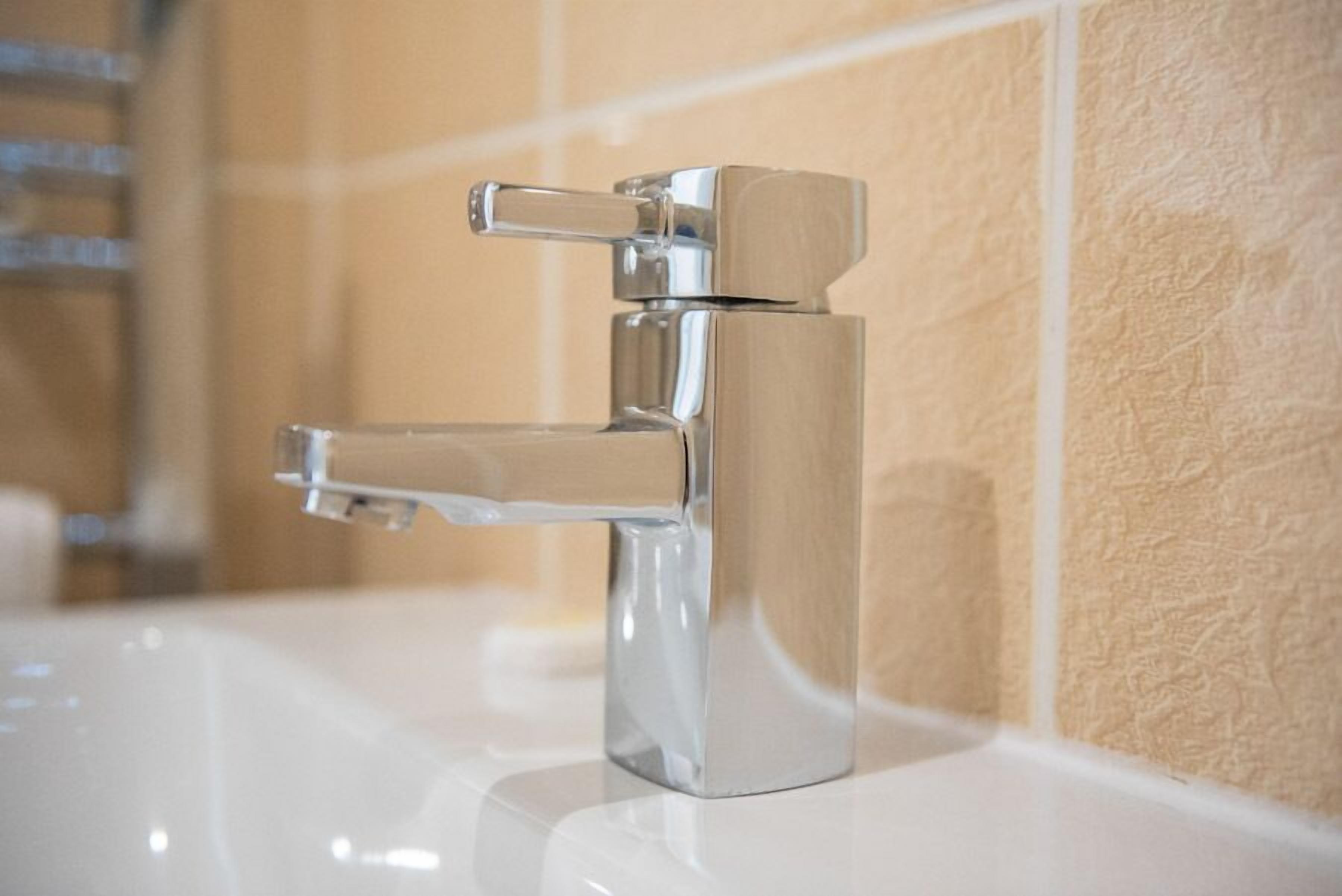 Un grifo cromado en un lavabo blanco, con una pared beige texturizada de fondo.