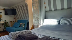 Une chambre d’hôtel avec un lit, un fauteuil bleu, une télévision et un élément de décoration servant de séparation.