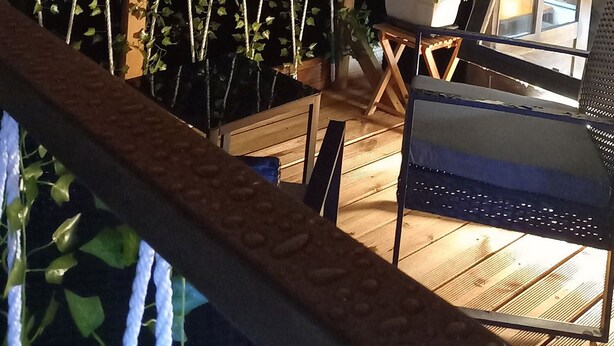 Une terrasse en bois agrémentée d’une structure suspendue pour les plantes, une petite table avec un pot de fleurs et une chaise.