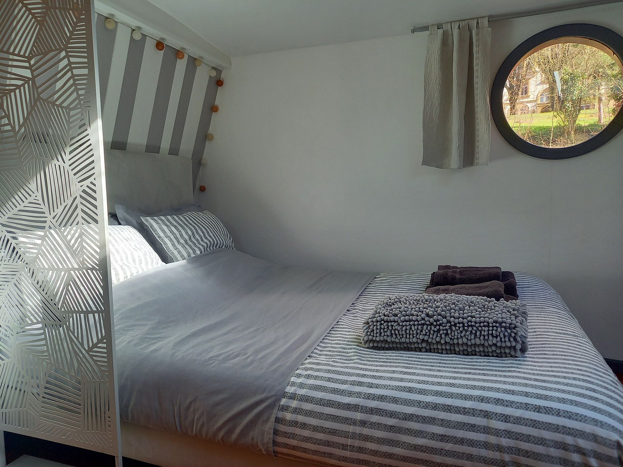 Un dormitorio con cama, almohadas, una ventana con vistas y un separador decorativo.
