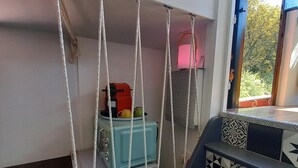 Un escalier aux marches décorées mène à une pièce où se trouvent une valise bleue, un appareil électroménager rouge et un rideau à motifs.