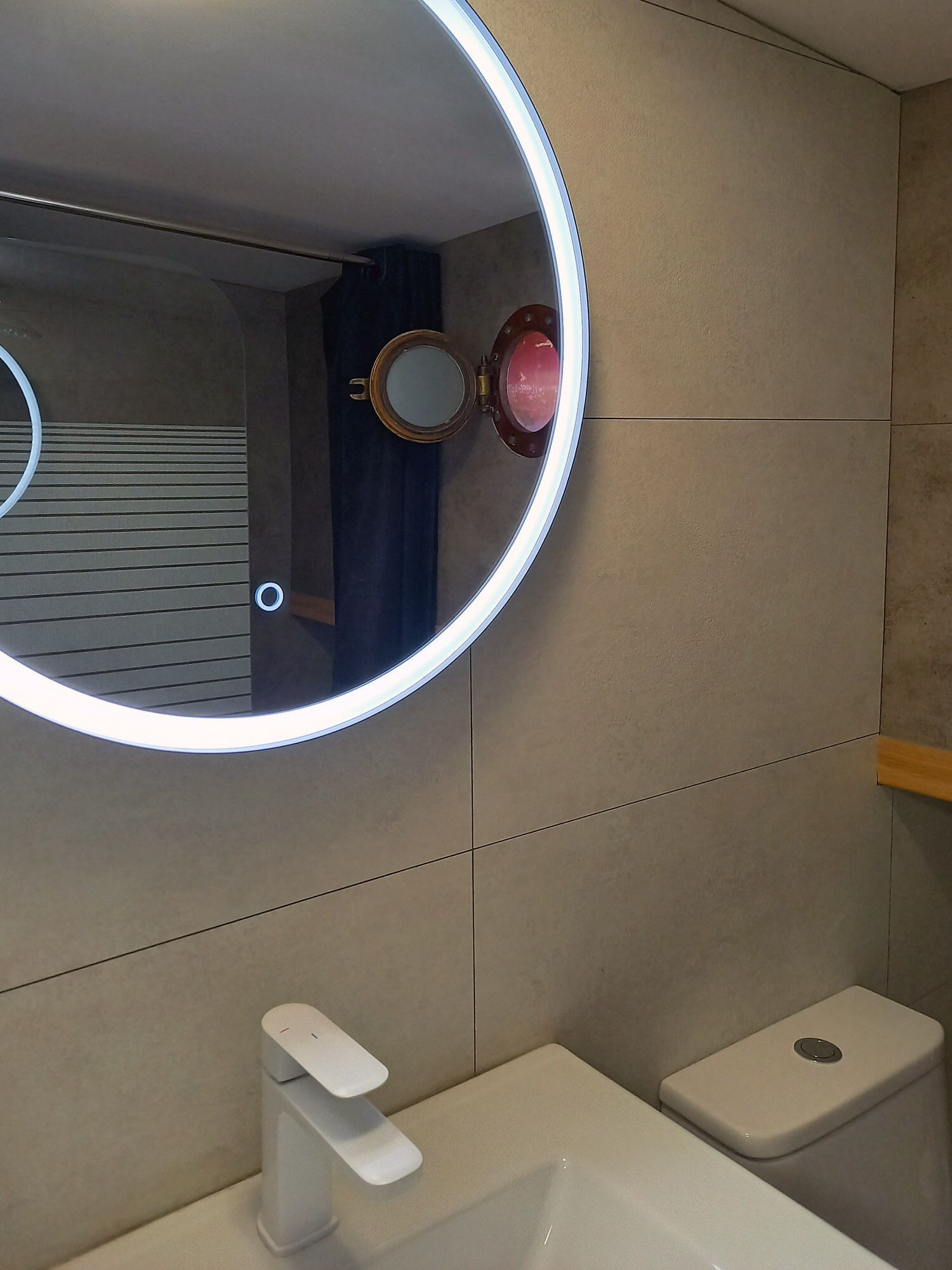 Une salle de bain avec un miroir rond, un lavabo blanc et des toilettes.