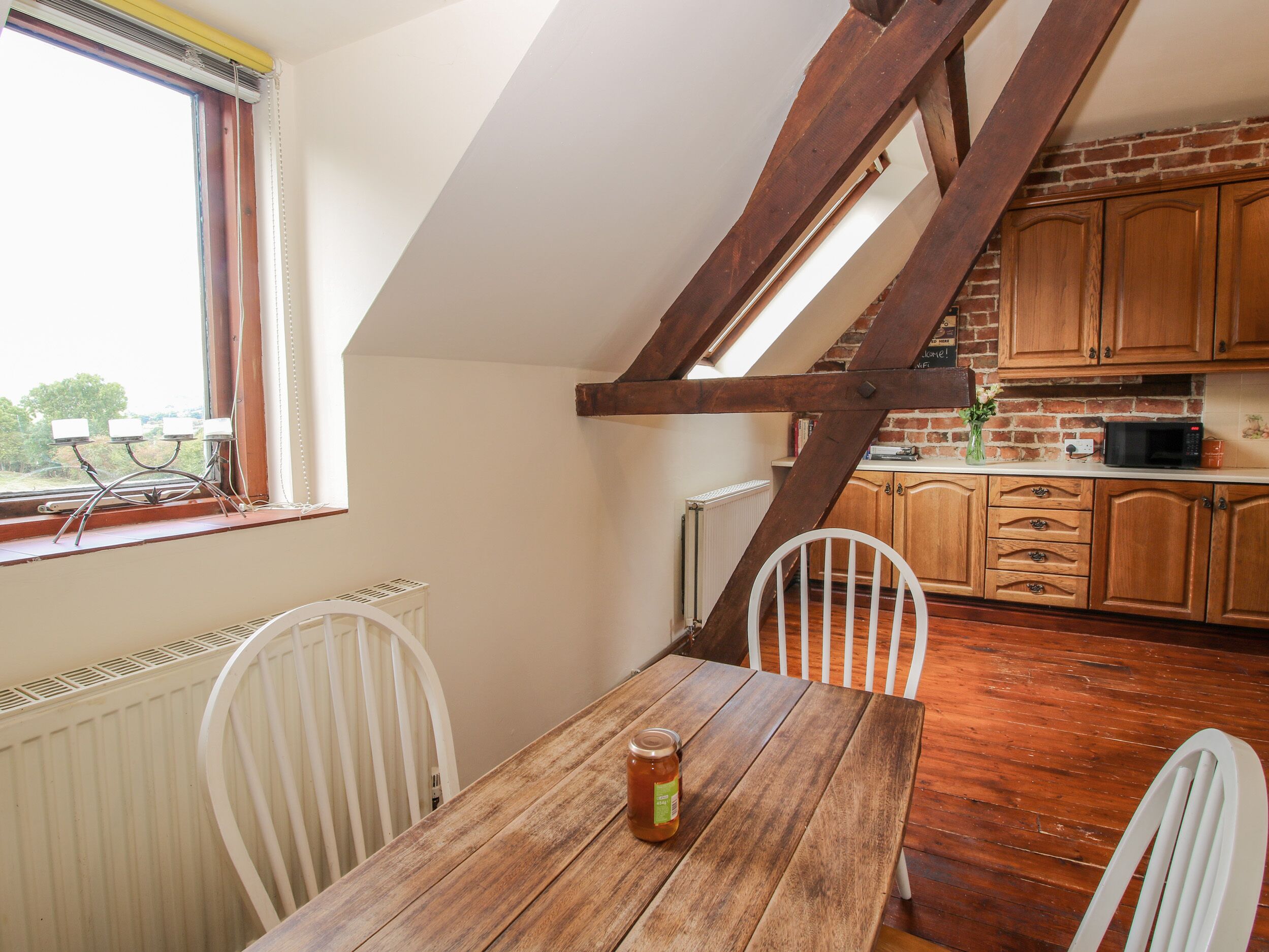 Een keuken met houten kastjes, een eettafel met stoelen en een raam met een radiator eronder.