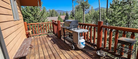 Une terrasse en bois avec un barbecue, une table en métal et un banc.