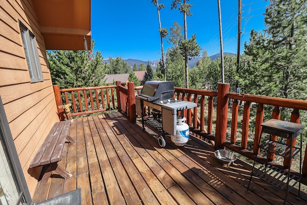 A wooden deck with a grill, a metal table, and a bench.