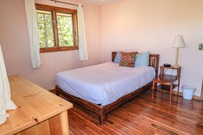 Une chambre avec un lit en bois, une table de chevet en bois avec une lampe, une fenêtre avec des rideaux et un bureau en bois.