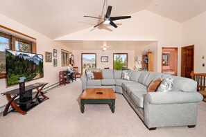 A spacious living room with a sectional sofa, a television, a piano, and a ceiling fan.
