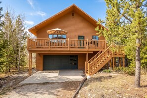 A two-story wooden cabin with a balcony, a garage, and a staircase leading to the upper level.