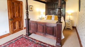 Un lit à baldaquin avec une tête de lit en bois, deux tables de chevet avec des lampes, un tapis rouge à motifs et une porte en bois.