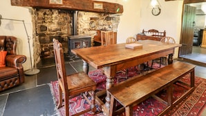 Un coin repas rustique avec une table et des bancs en bois, des murs en pierre et une cheminée traditionnelle.