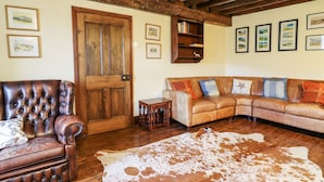 Une pièce avec une porte en bois, un fauteuil en cuir, un canapé, une petite table et un tapis en peau de vache.