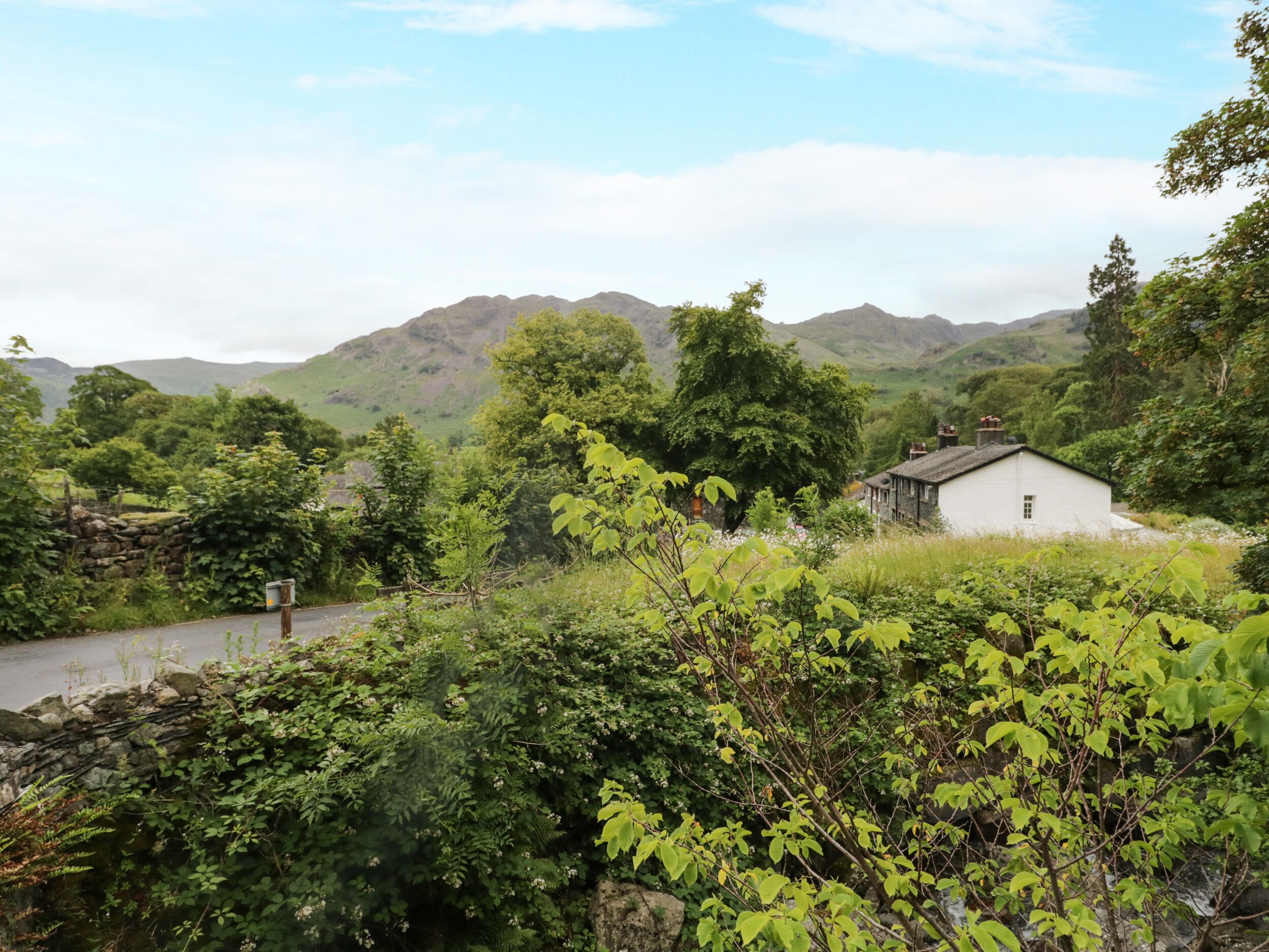 Un paisaje rural con una casa blanca, abundante vegetación y montañas al fondo.