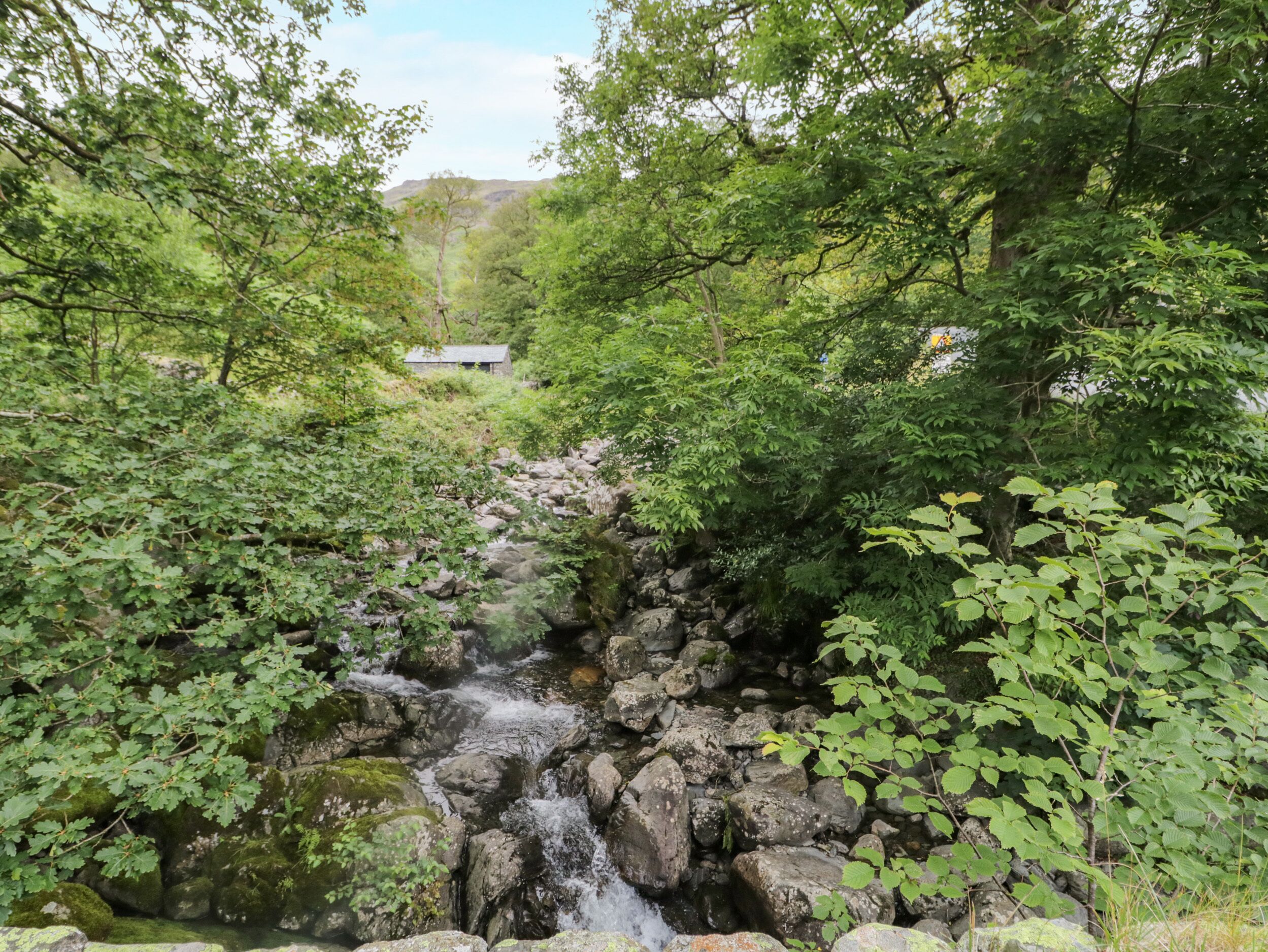 Paisaje natural con una cascada pequeña rodeada de vegetación exuberante y una estructura de piedra al fondo.