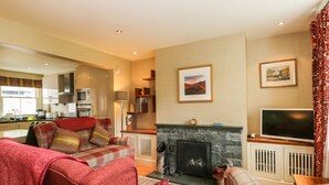 Una sala de estar con chimenea, televisor y comedor, con una cocina al fondo.