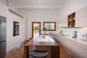 A modern kitchen with a central island, white cabinetry, and a view of the outdoors through windows.