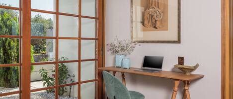 Et værelse med et træskrivebord, en bærbar computer, en vase med blomster og et indrammet kunstværk på væggen.