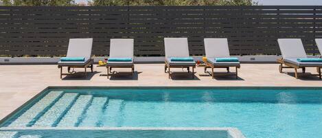 A pool area with four lounge chairs and a black fence in the background.
