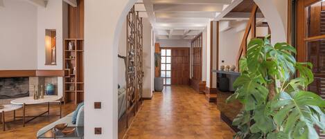 A spacious hallway with a wooden floor, a seating area with a table and chairs, and a large potted plant.
