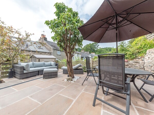Un espace patio aménagé avec un canapé en osier, une chaise en treillis et une table placée sous un grand parasol.