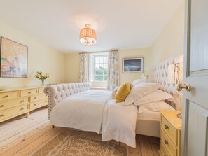Une chambre à coucher avec un grand lit, une commode, une table de chevet, une fenêtre avec des rideaux, un lustre et un tableau au mur.