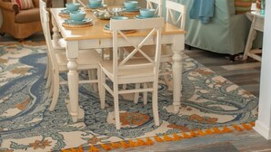 A dining area with a wooden table and white chairs, a patterned rug, and a blue and white color scheme. - Comfortable and clean beach cottage convenient access to the beach. (Kitty Hawk)