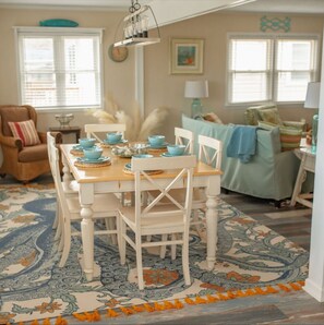 Un espace repas avec une table en bois et des chaises blanches, un tapis à motifs et une décoration aux couleurs bleu et blanc.
