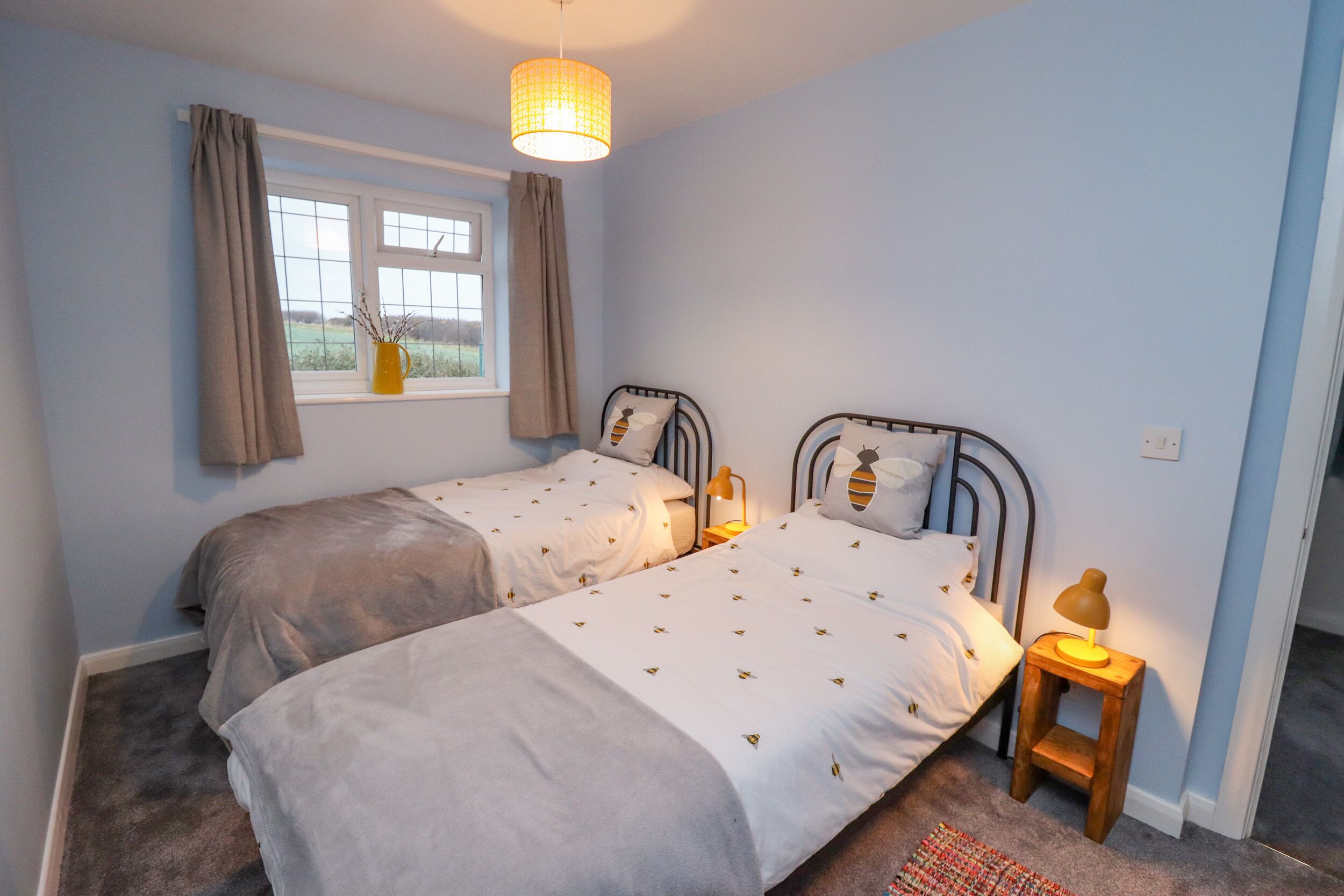 Un dormitorio con dos camas individuales, una ventana con cortinas, una lámpara de noche y vistas al exterior.