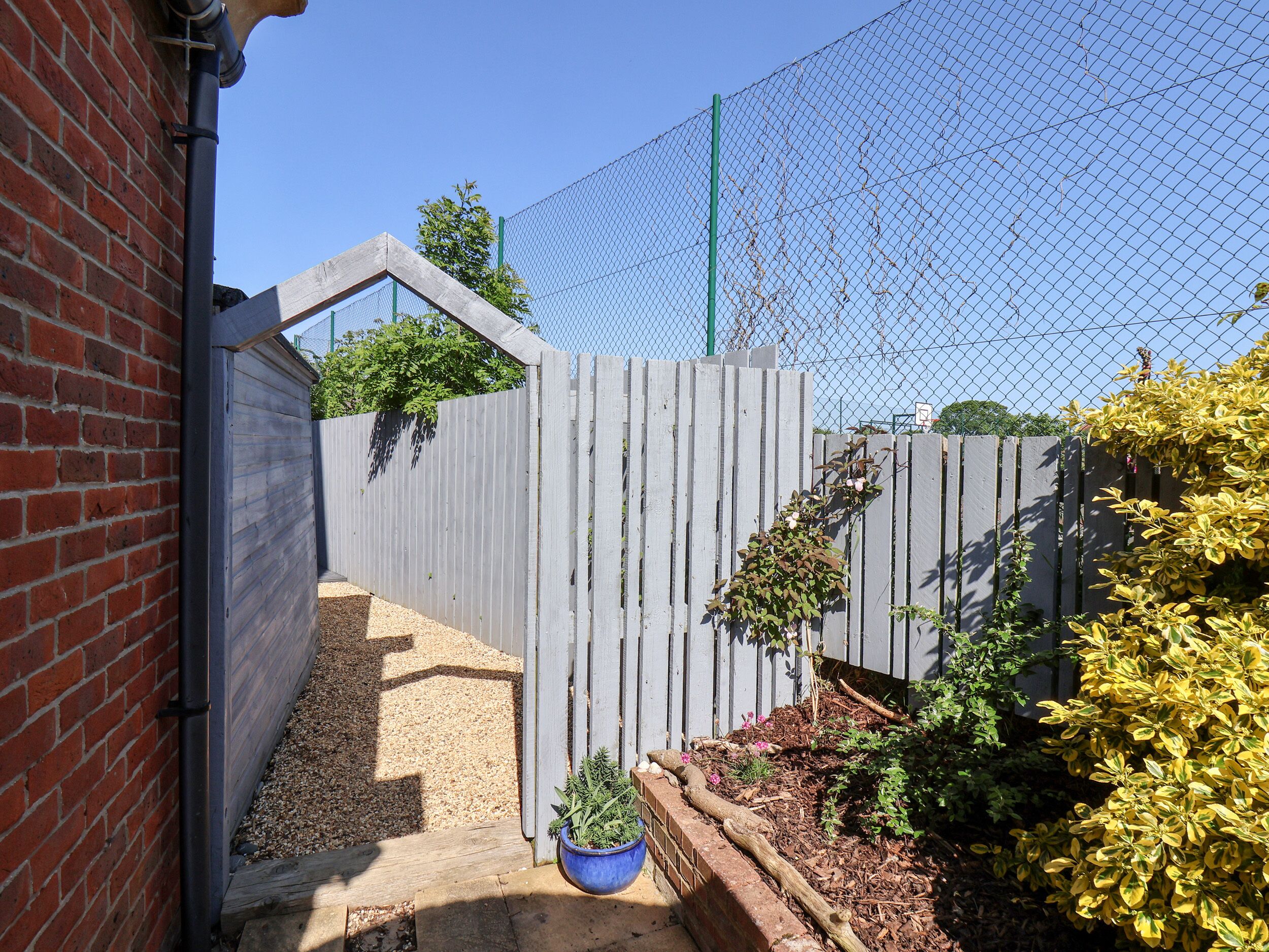 A fenced garden area with a wooden fence, gravel path, and various plants.