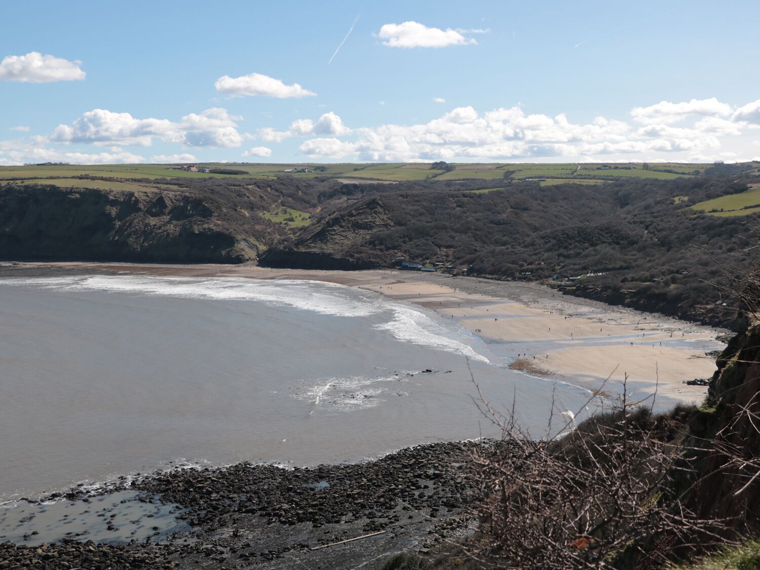 A coastal landscape with a beach, cliffs, and a clear sky.
