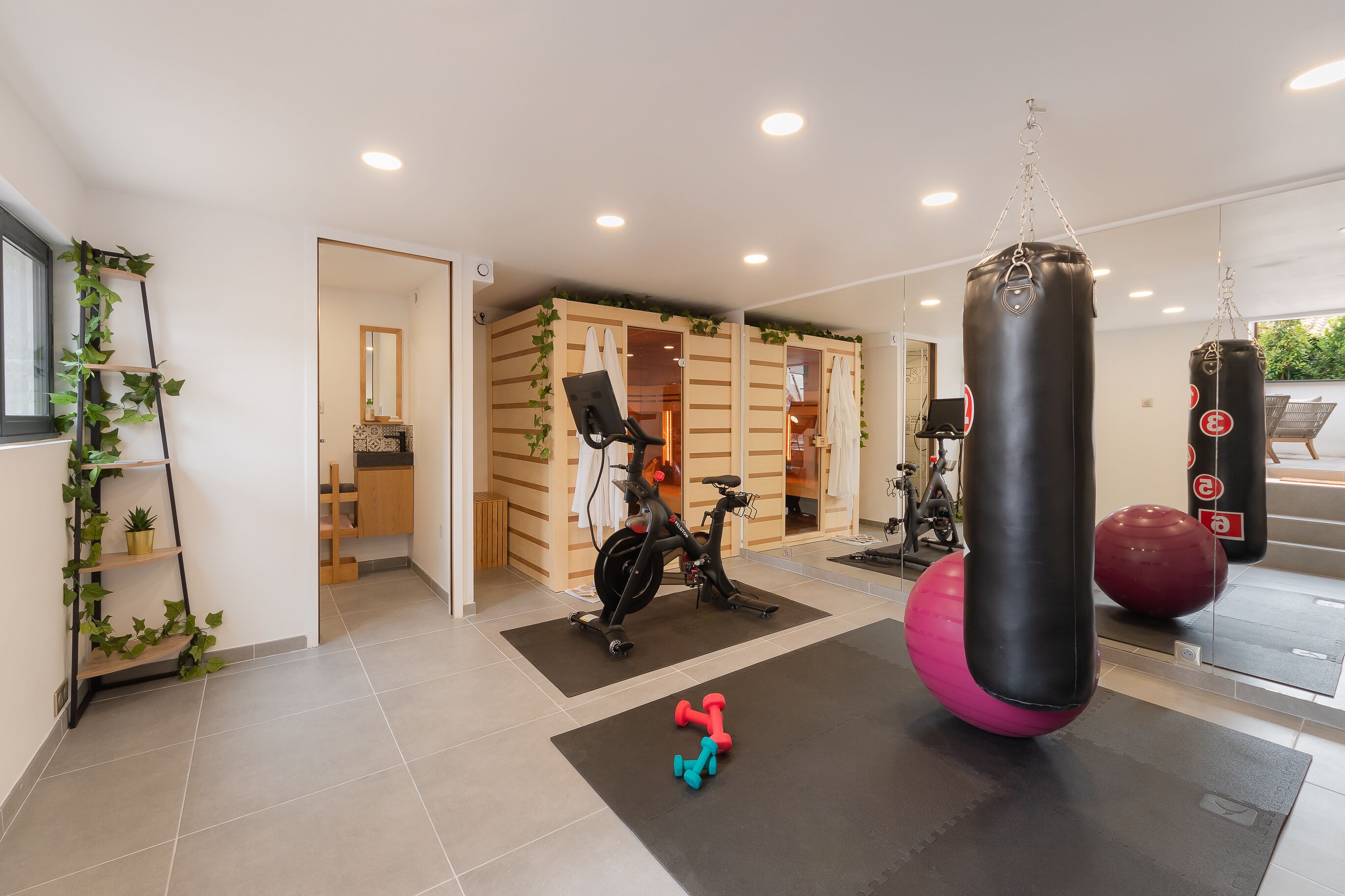 Een sportschool thuis met fitnessapparatuur, waaronder een bokszak, trainingsballen en gewichten.