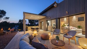Un patio exterior con diseño de casa moderno, que incluye una zona de estar con sofás y sillones, una mesa de comedor y un pozo de fuego.