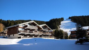 Una chaleta de varios pisos con balcones, frente a un paisaje montañoso nevado.